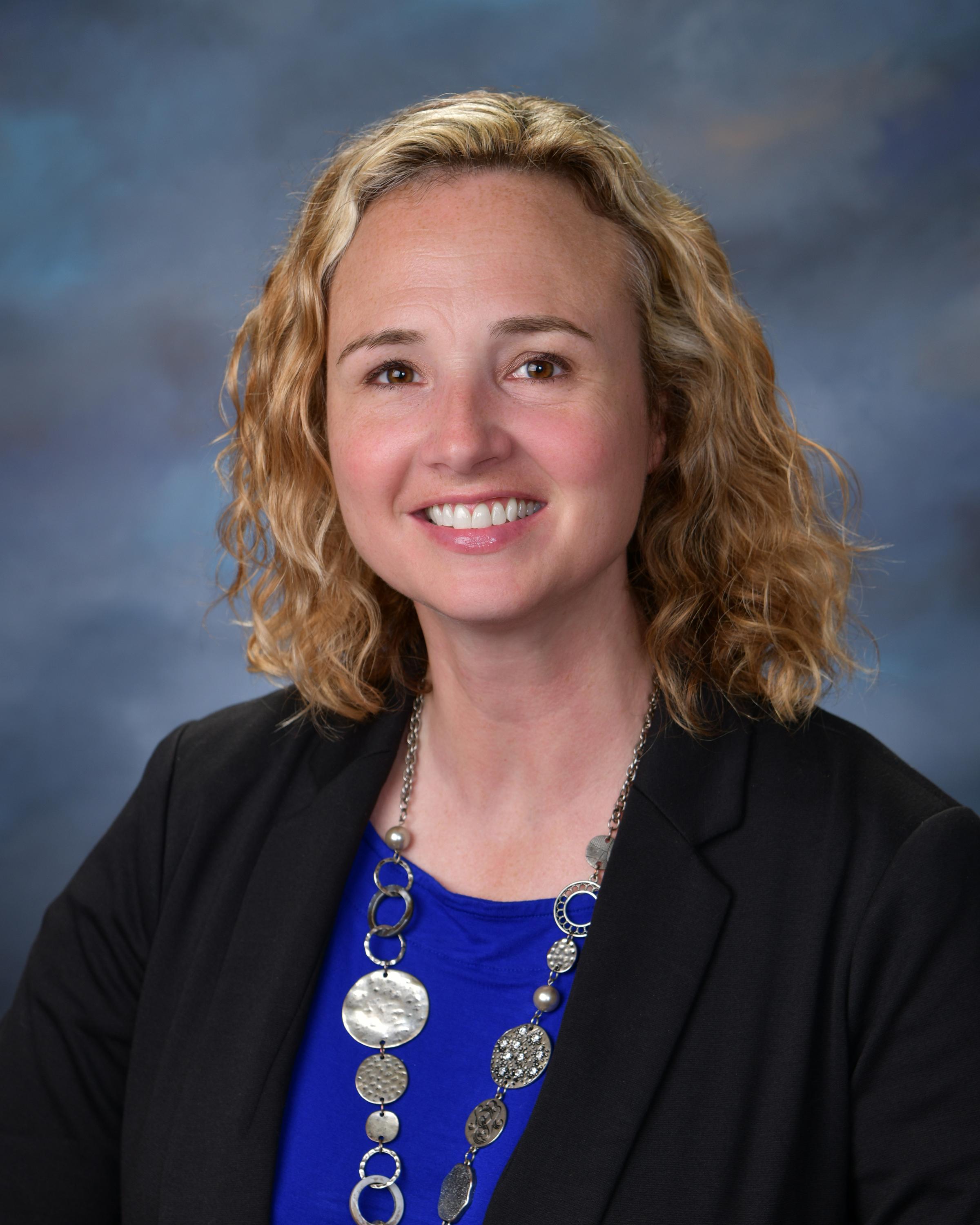 Profesional Headshot of Sarah Chivington: blond hair female with blue shirt, black blazer and silve necklace